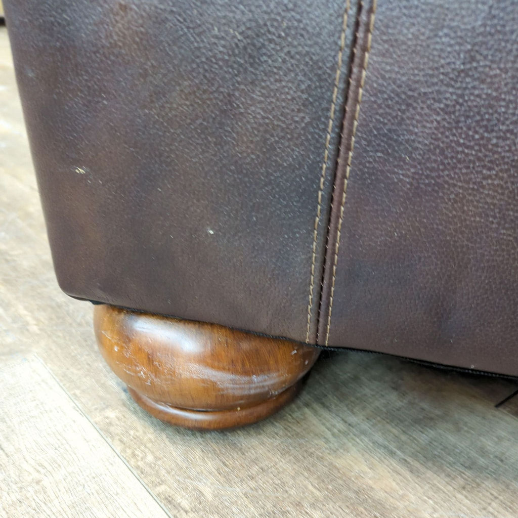 Close-up of brown leather chair's wood foot, highlighting its sturdy design.