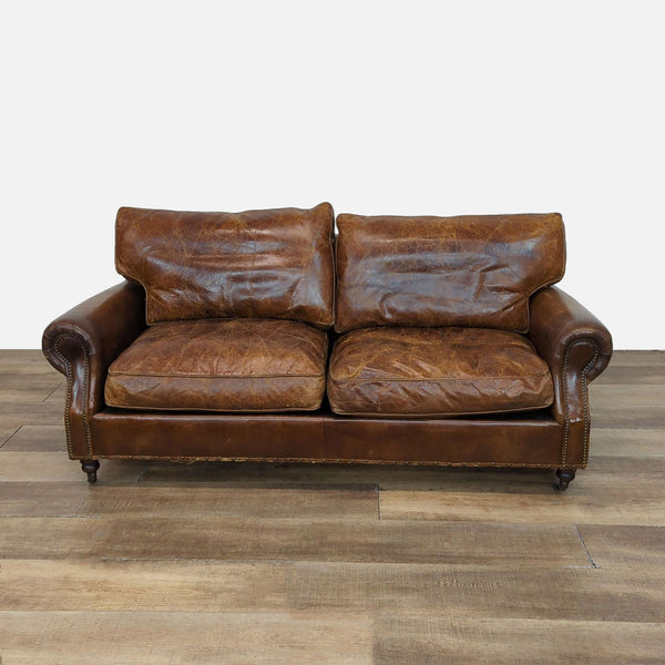 Distressed leather loveseat with nailhead trim and rolled arms on wood feet.