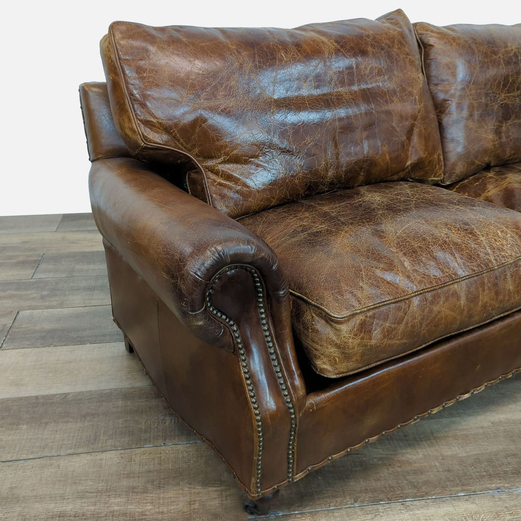 Close-up of a Reperch loveseat arm, exhibiting distressed leather and nailhead details.