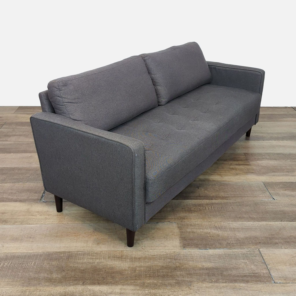 Side view of a gray upholstered loveseat showing tufted seat and sleek armrests.