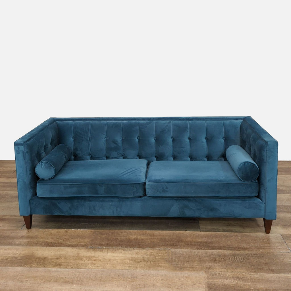 Three-seat blue tufted sofa with removable cushions and tapered wood legs.