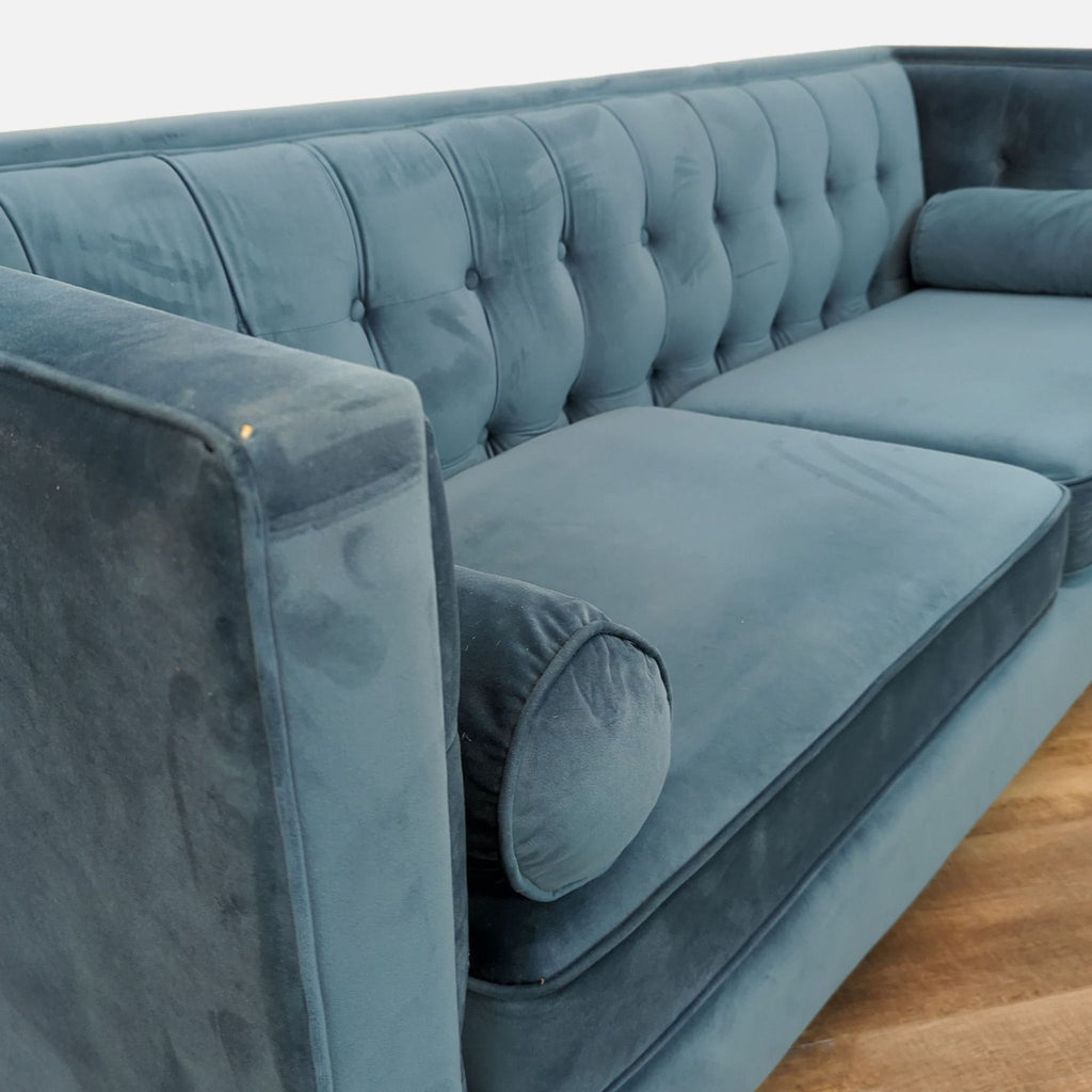 Side view of blue Chesterfield-style sofa with bolster pillows and geometric design.
