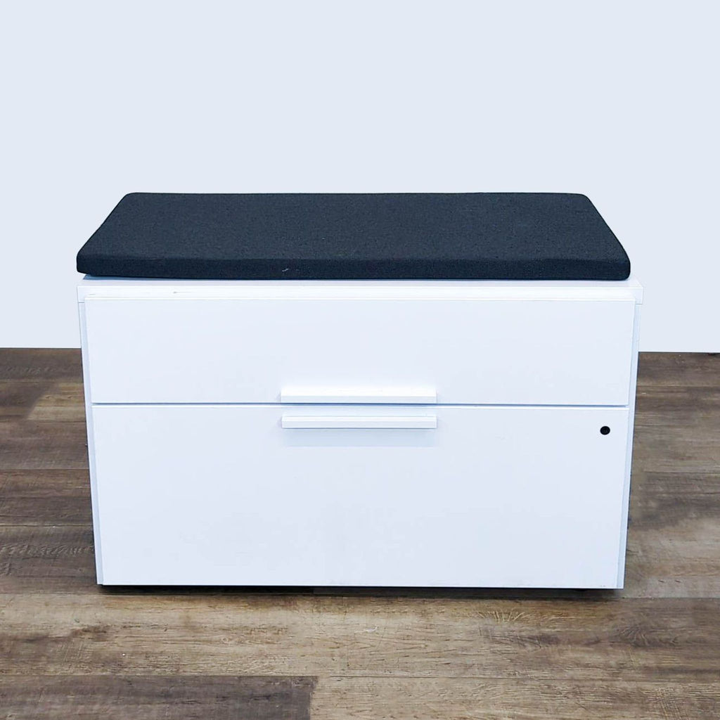 Knoll white cabinet with black cushioned top on wooden floor.