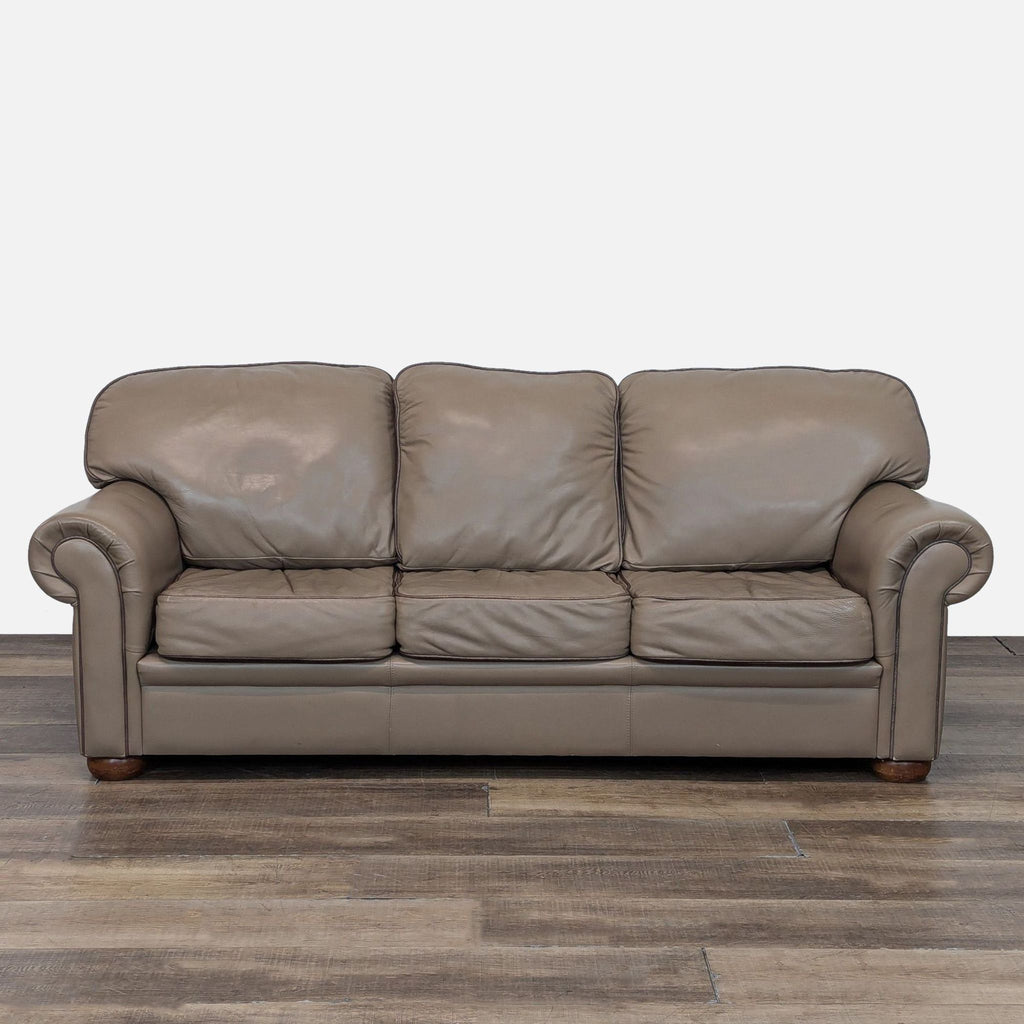 Taupe leather sofa with rolled arms and wooden legs, front view.