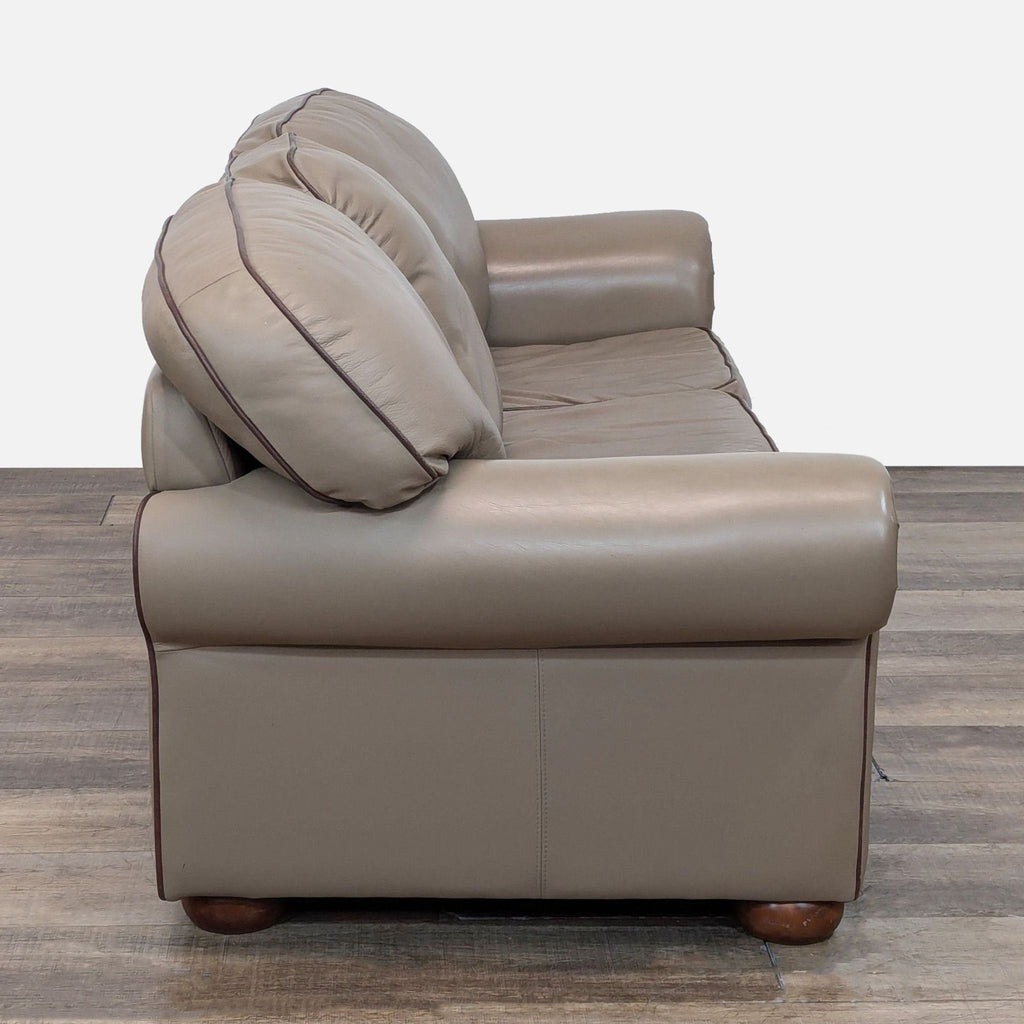 Side view of a taupe leather sofa with plush cushions and wooden feet.