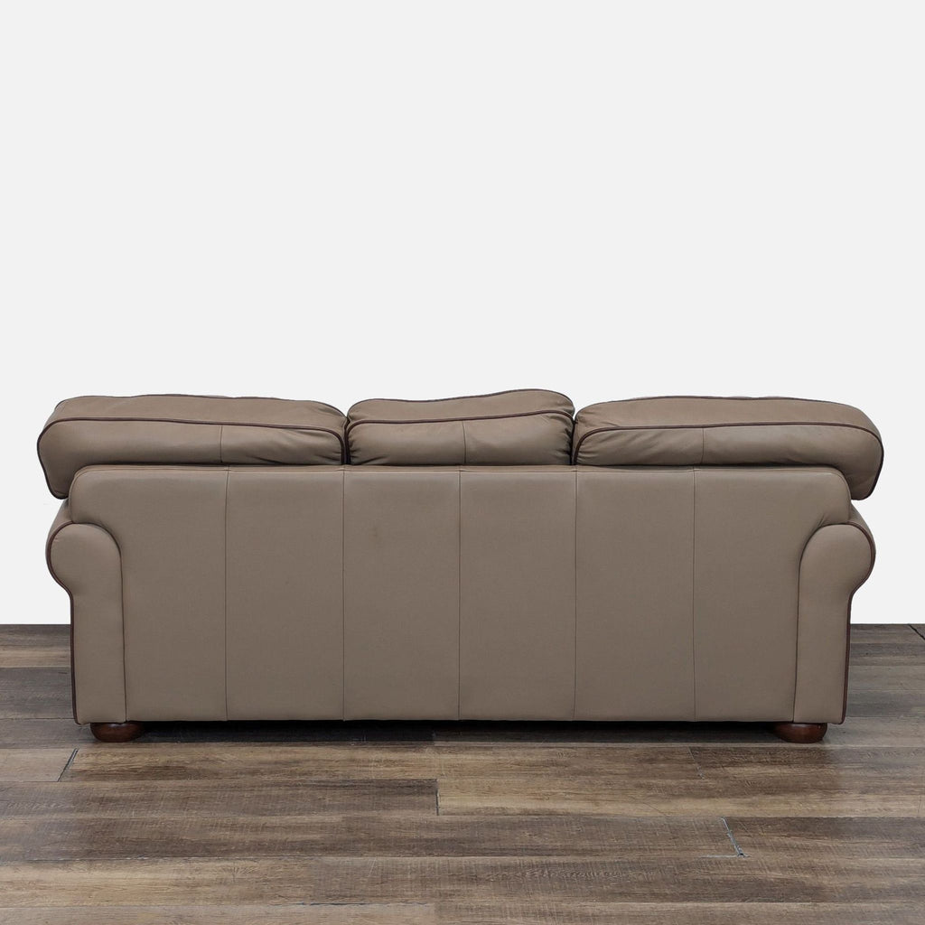 Back view of a taupe leather sofa showing smooth texture and rolled arms.