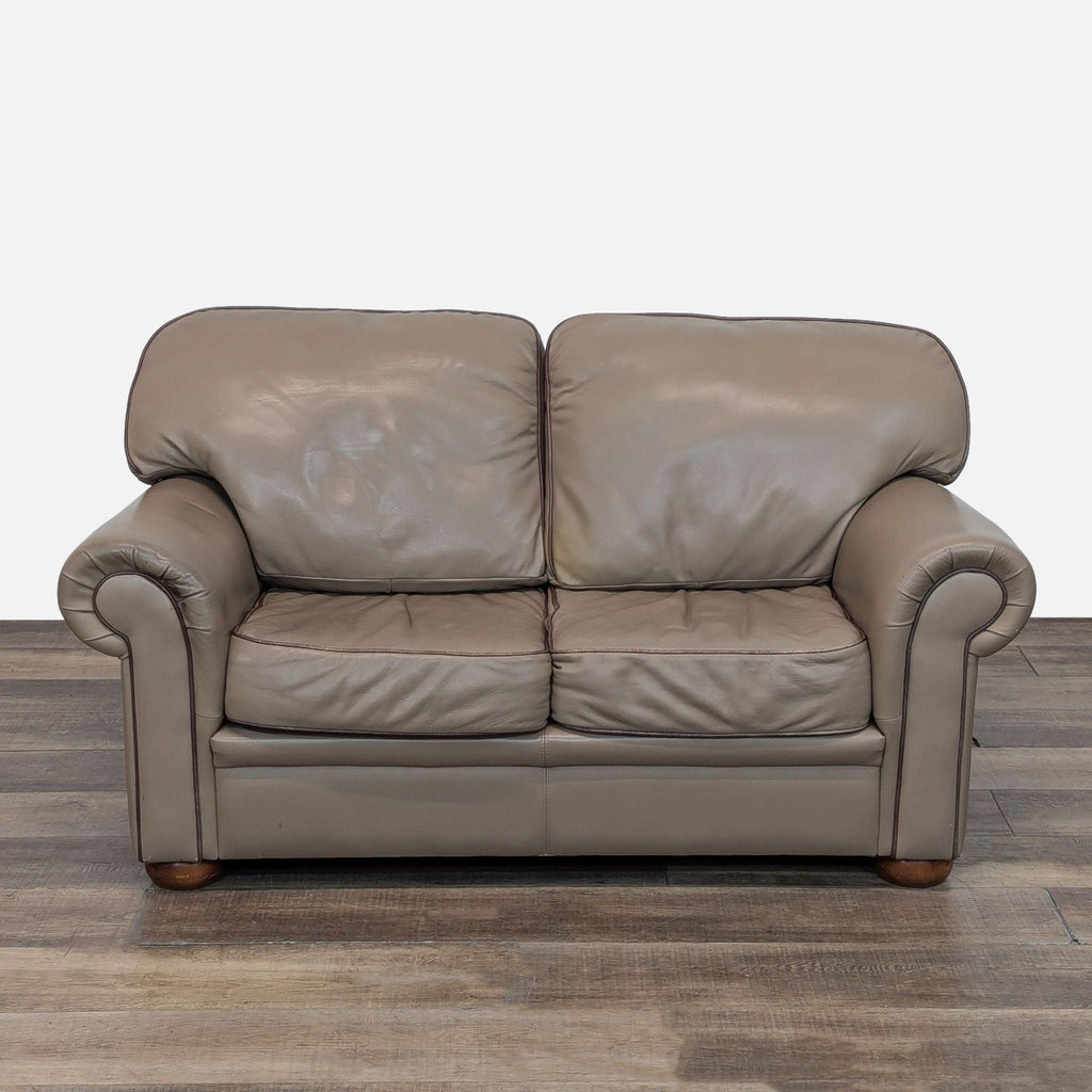 Taupe leather loveseat with rolled arms and wooden feet.