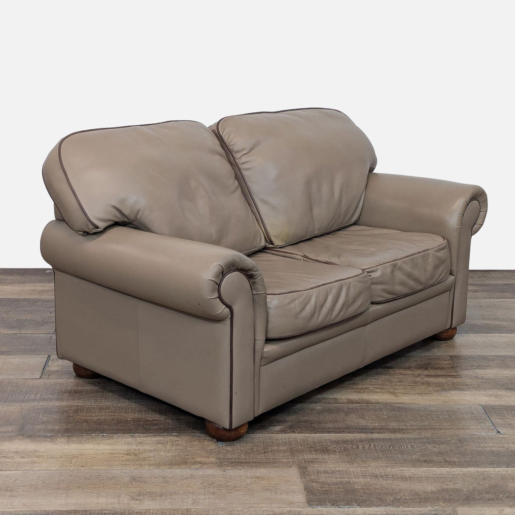 Angled view of taupe leather loveseat featuring rolled arms.