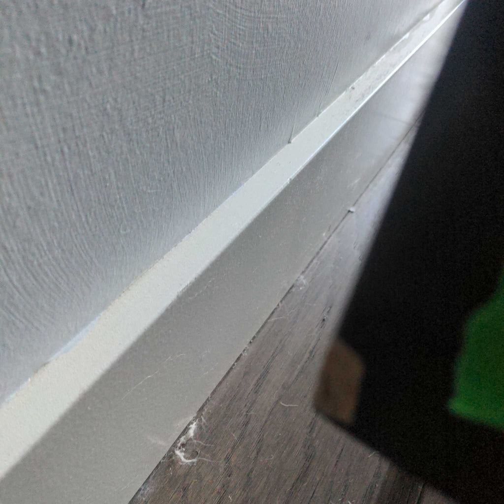 Close-up view of entertainment center side and wall, highlighting baseboard and flooring details.