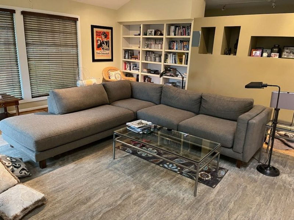 1. Modern gray Reperch sectional sofa arranged in a cozy living room with shelves, art, and a glass coffee table.  