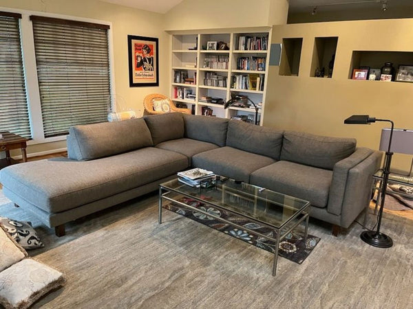 1. Modern gray Reperch sectional sofa arranged in a cozy living room with shelves, art, and a glass coffee table.  
