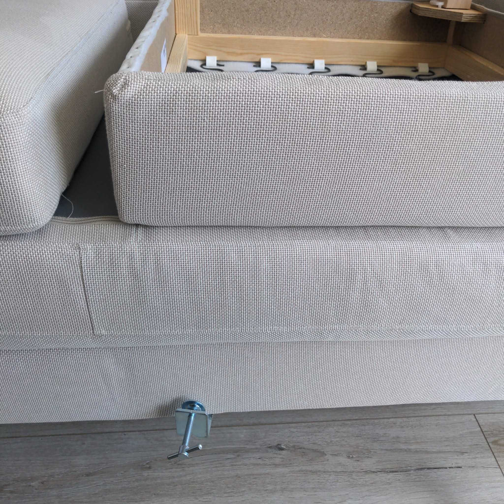 1. Close-up of a beige sectional sofa showing its inner frame and connecting hardware on a wooden floor.