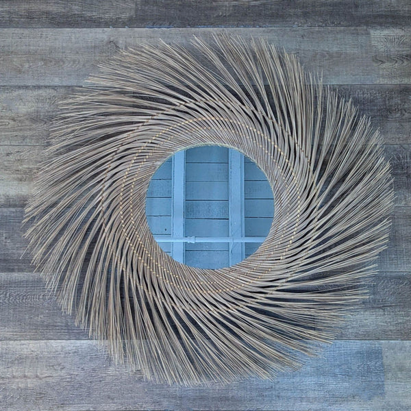 Round mirror with handwoven coconut fronds frame, on wooden floor.