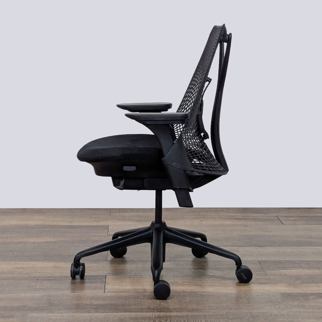 Profile angle of a Sayl chair, highlighting the flexible mesh back and cushioned seat, on a wooden surface.