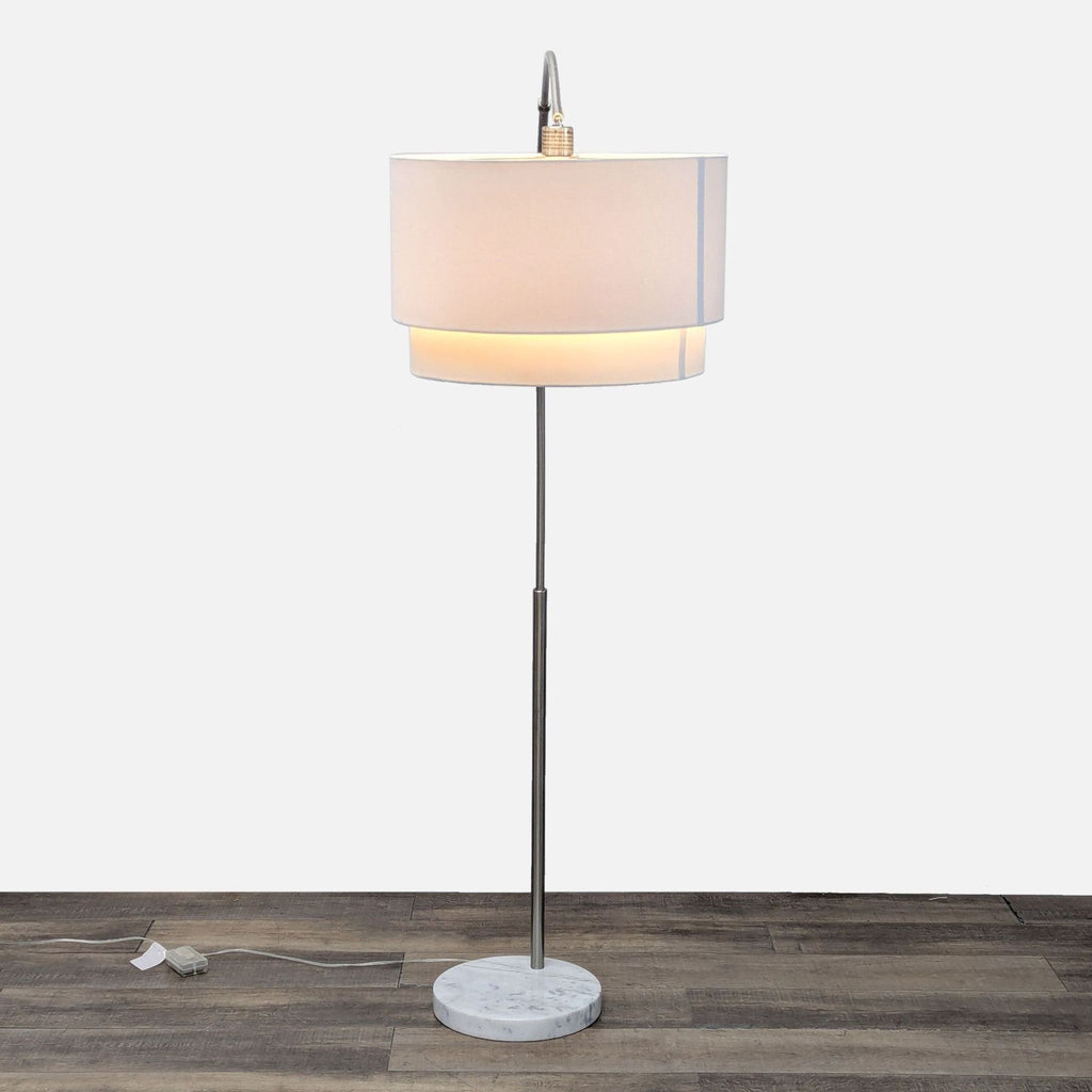 Sleek floor lamp with a metal arm, fabric shade, and marble base on a wooden floor.