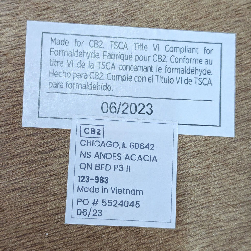 Product labels with compliance and manufacturing details for a CB2 Acacia bed, made in Vietnam.