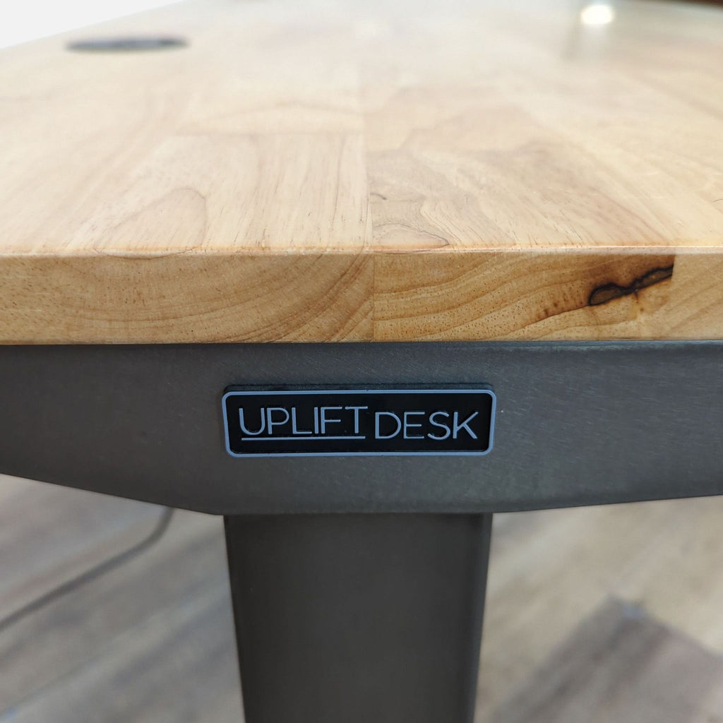Focus on Uplift Desk logo on a wooden desk with metal legs.