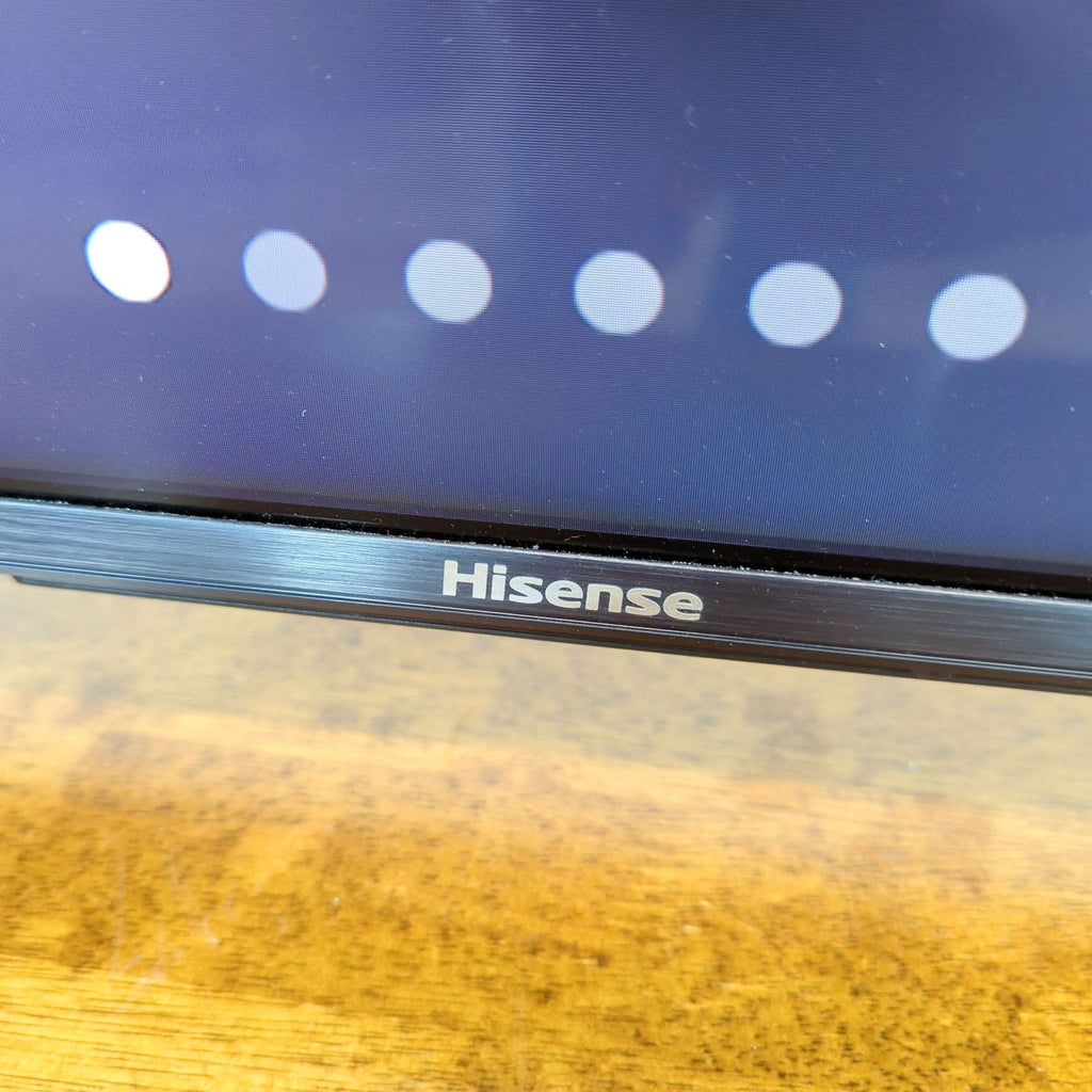 Close-up of Hisense logo on the bezel of the 55" Mini-LED TV, with screen and table visible.