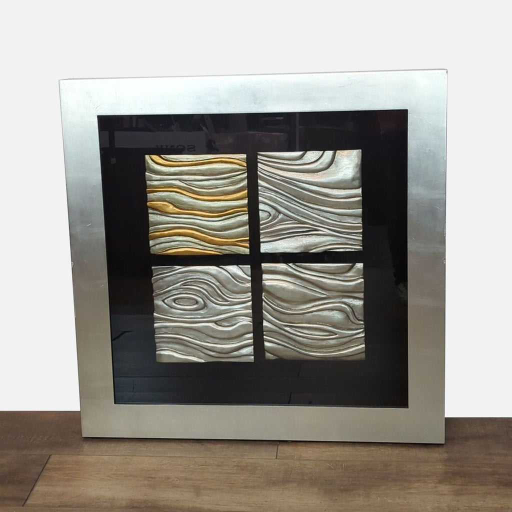 Framed wall panel with four textured squares; one gold, three silver-grey.