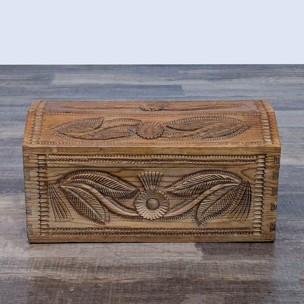 Intricately carved wooden trunk, closed with floral details, on a wooden floor.