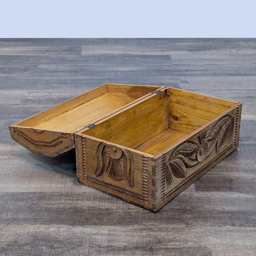 Open wooden trunk with detailed carvings, showing spacious interior on wooden floor.
