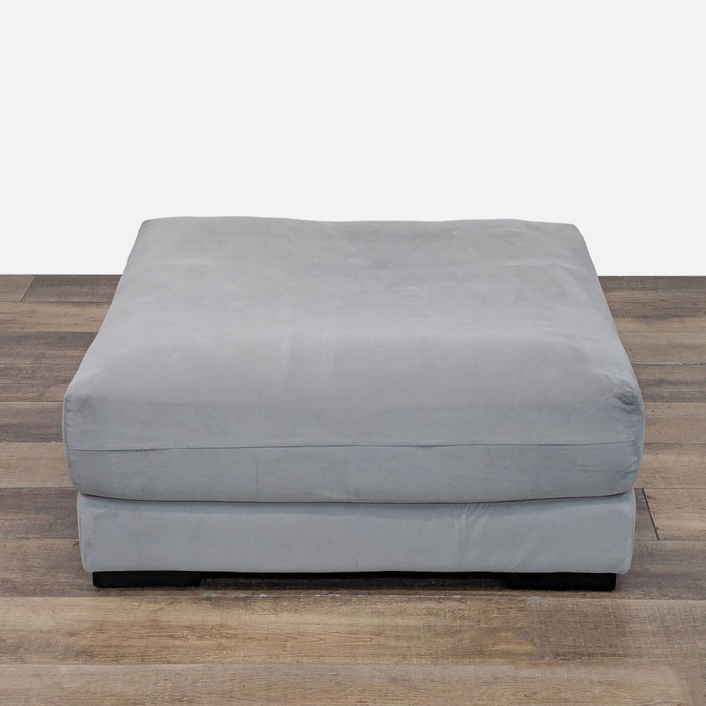 West Elm ottoman in soft silver velvet, shown on a wood floor.