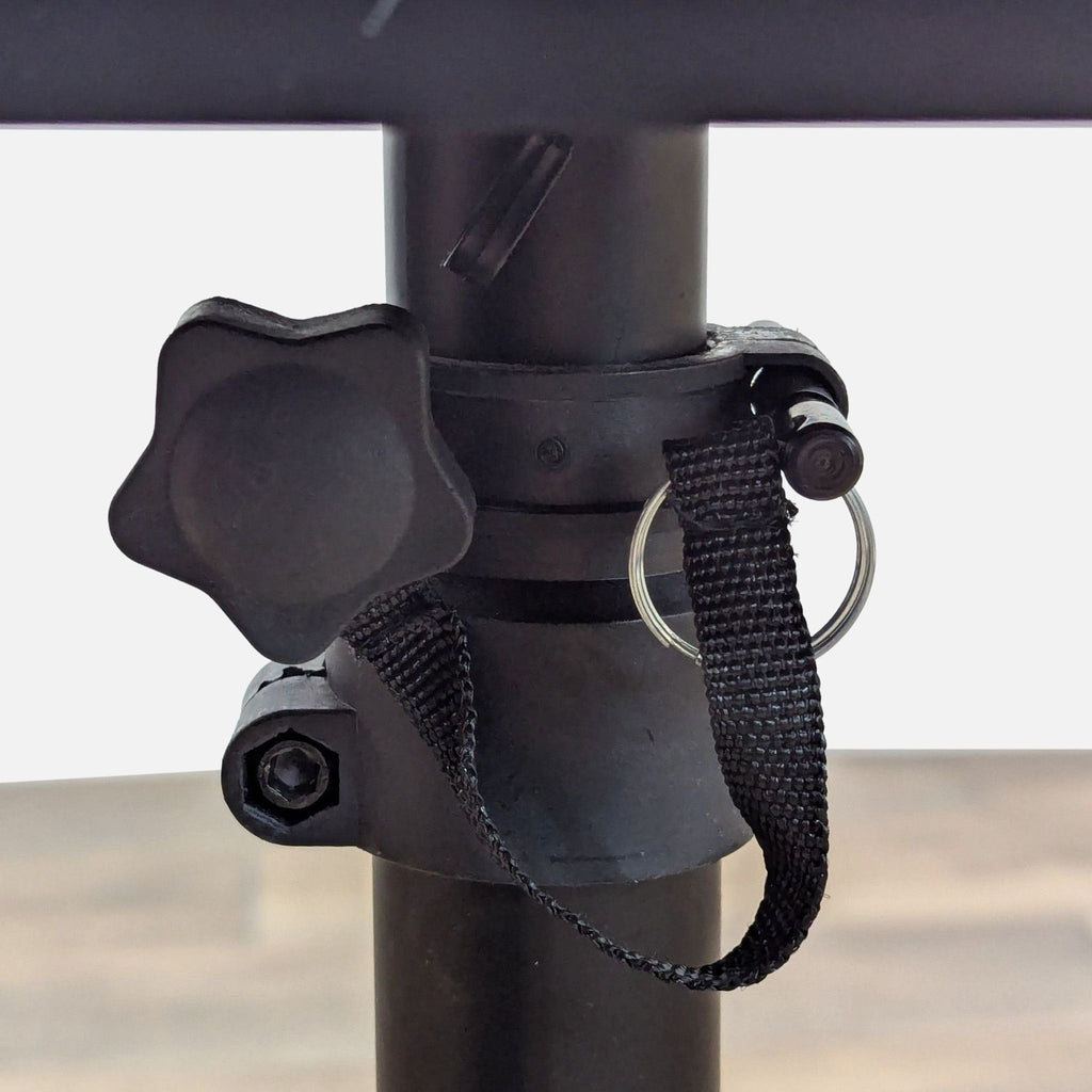 Close-up of adjustable mechanism and knob on black speaker stand.
