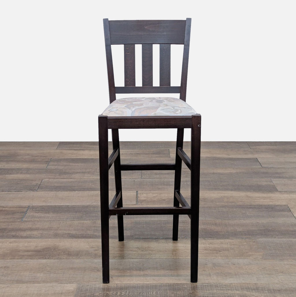 Dark wooden bar stool with a patterned cushion seat on a wooden floor.