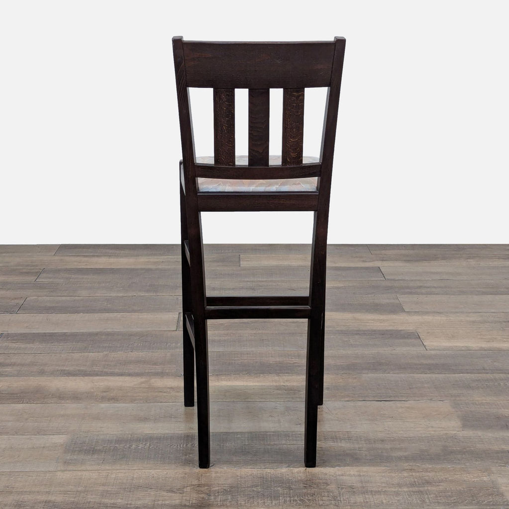 Rear view of dark wooden stool with slatted backrest, showing cushioned seat on a wooden floor.