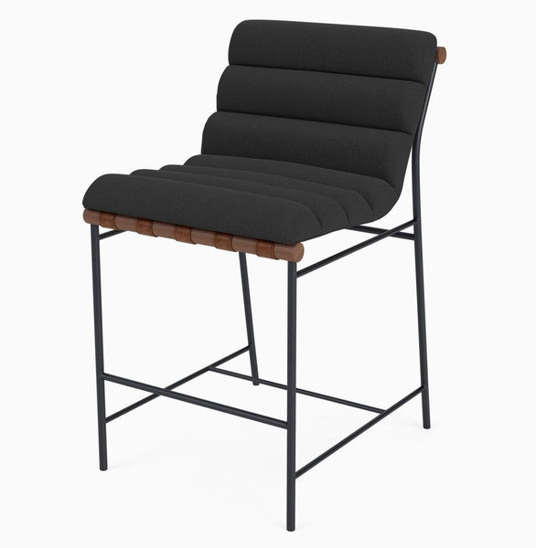 Modern stool with charcoal boucle upholstery, leather straps, and a sturdy metal frame.
