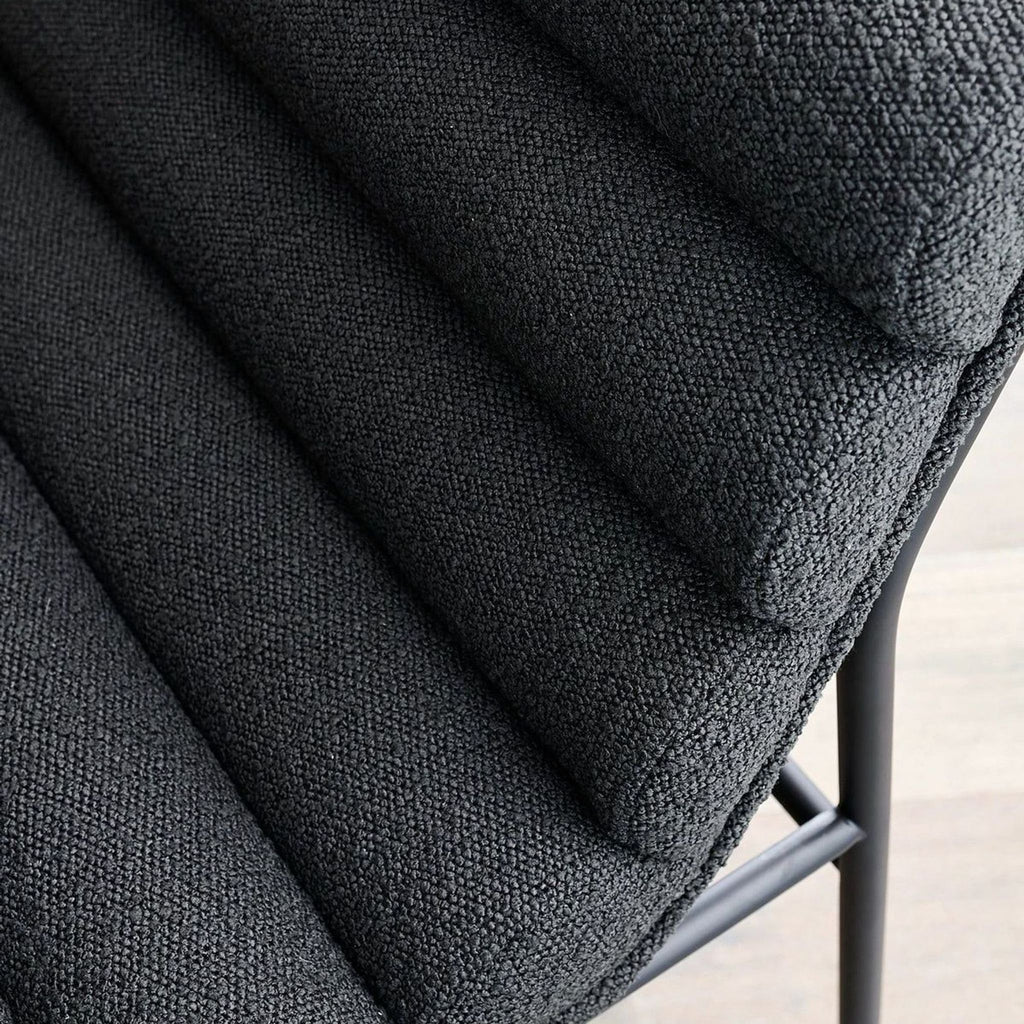 Close-up of charcoal boucle upholstery with channel-tufted design on a modern stool.