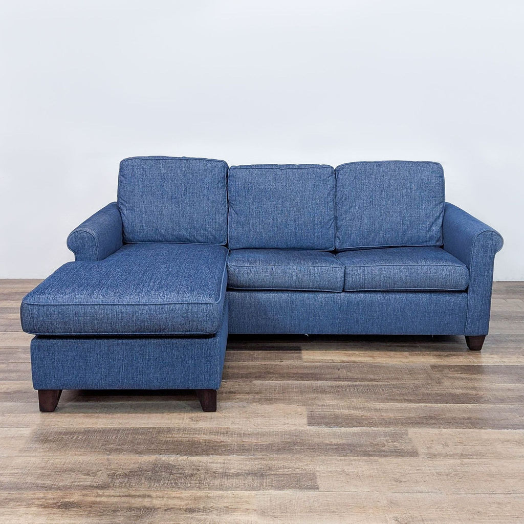 Blue sleeper sofa with reversible chaise and rolled arms on a wooden floor.