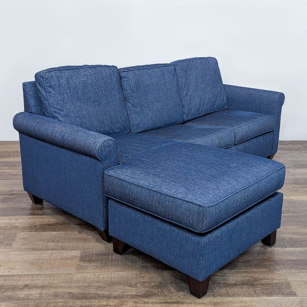Angled view of a blue sleeper sofa with chaise and wooden legs, showing rolled arms.