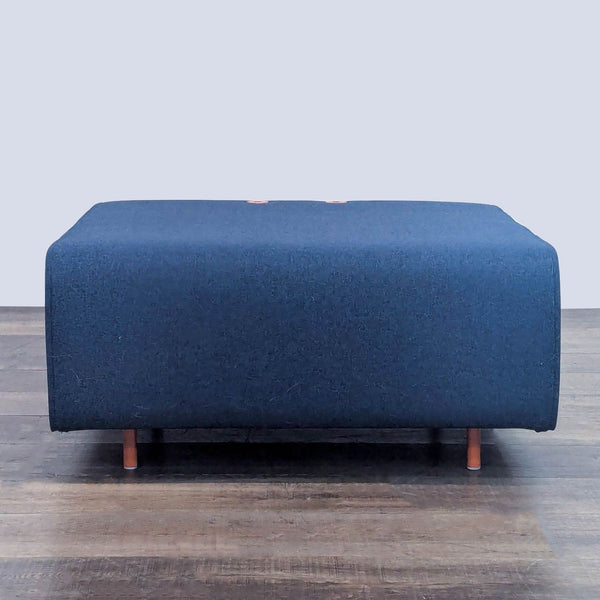 Navy blue ottoman with wooden legs on a wooden floor. 