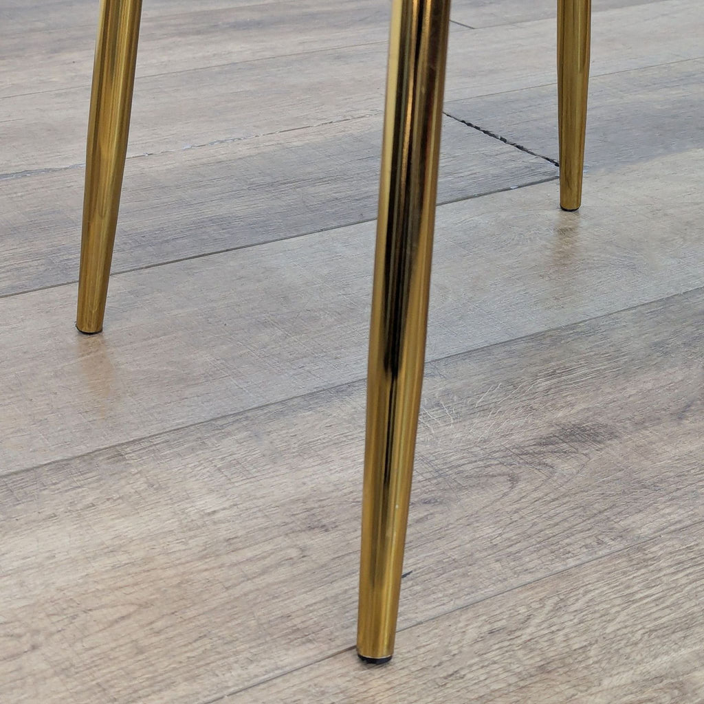 Close-up of the gold legs of a Reperch dining chair on wooden flooring.