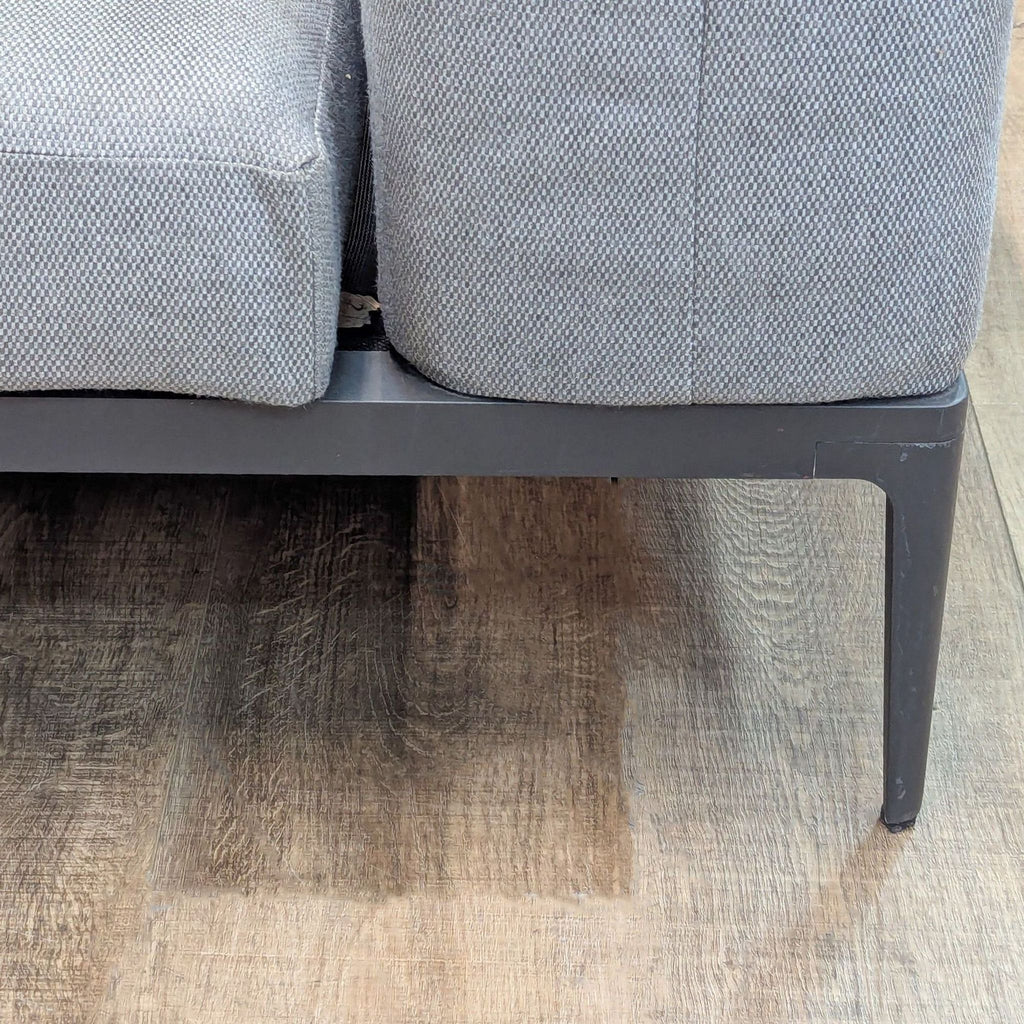 Detail of gray upholstered outdoor sofa on wooden floor.