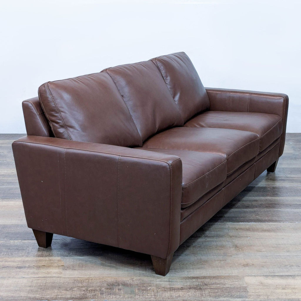 Angled view of 3-seat brown leather sofa, showing cushions and tapered legs.