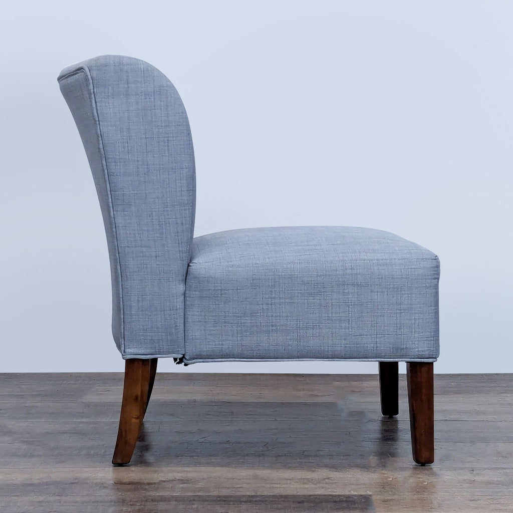 Side view of a gray linen upholstered slipper chair with wooden legs.