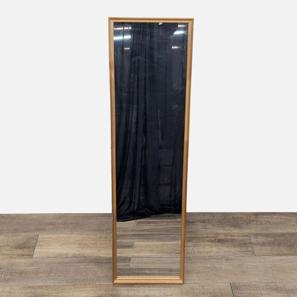 Full-length rectangular mirror with a wood frame, placed against a wooden floor.