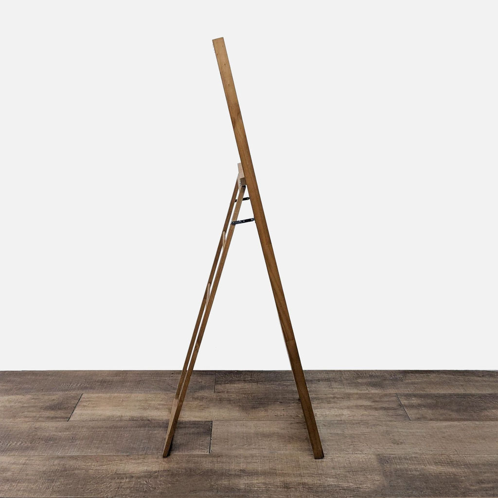 Side view of a rectangular mirror with a wooden stand and frame on a wooden floor.