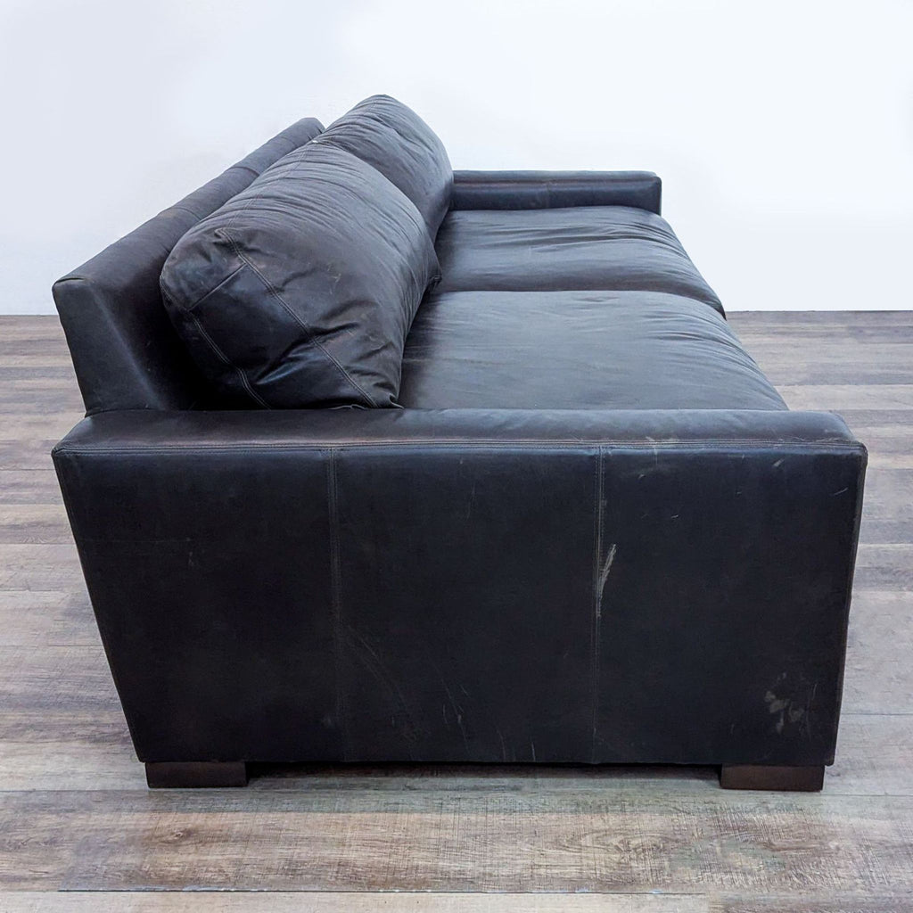 Side view of a black leather 3-seat sofa with robust wooden structure.