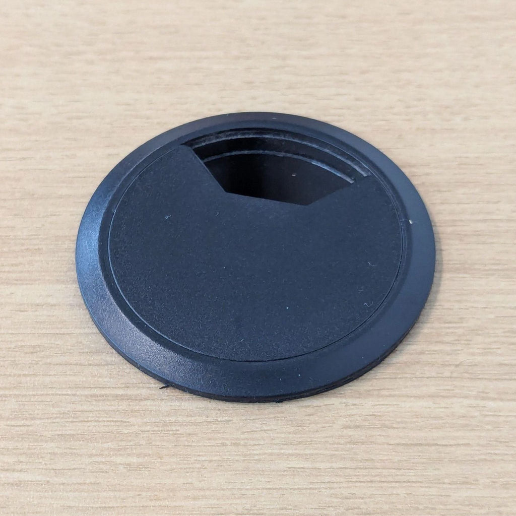 Close-up of a desk grommet on an oak laminate surface.