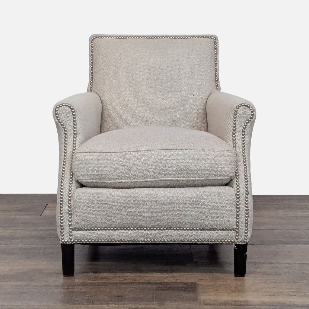 Beige lounge chair with dark wooden legs and nailhead trim.
