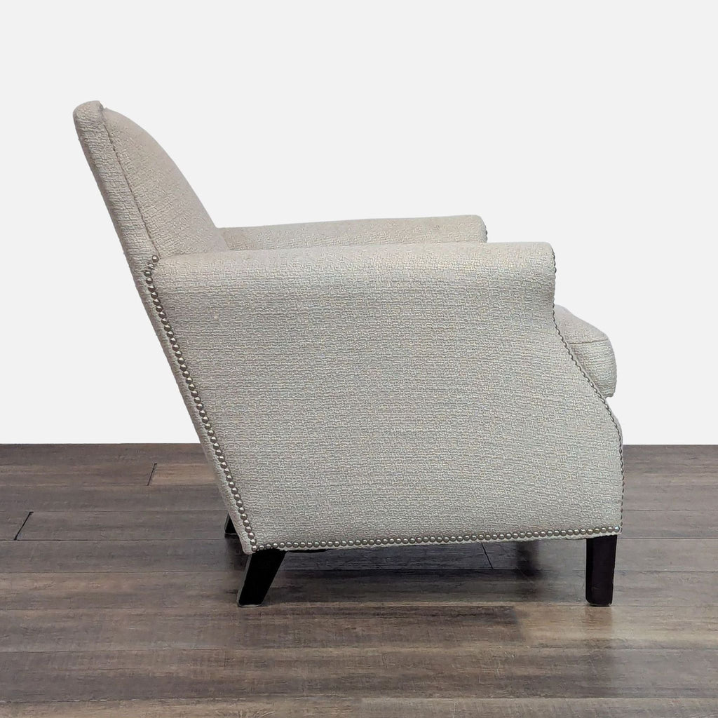 Side view of a beige chair, nailhead details, and dark legs.