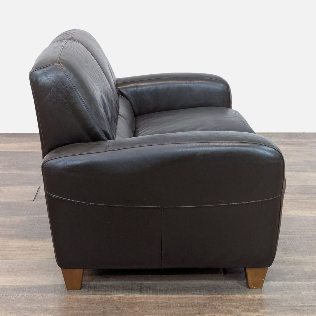 Side view of black leather loveseat with rounded arms and tapered wood feet.