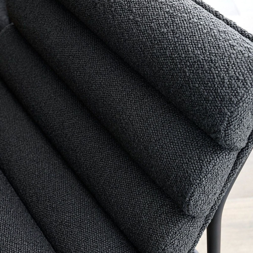 Close-up of channel-tufted charcoal boucle upholstery on a modern stool.