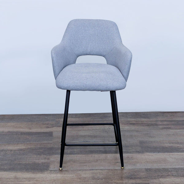 Gray upholstered bar stool with curved backrest and black metal legs on wooden floor.