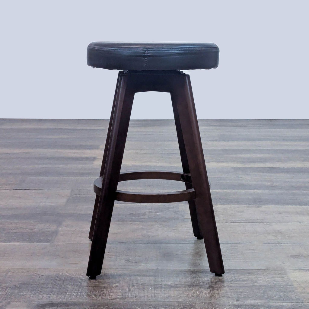Side view of stool with black seat, supported by dark brown wooden legs and base.