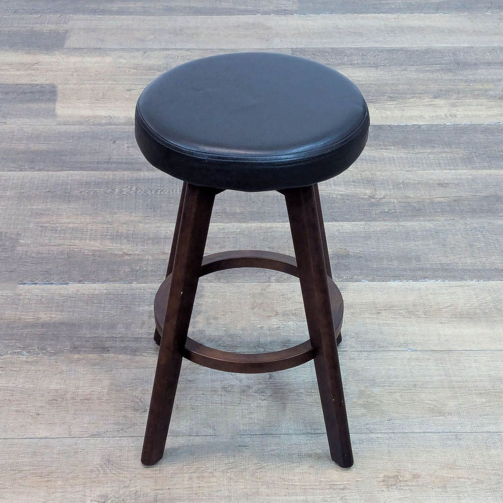 Top view of a black padded stool on dark wooden legs, set on a wood floor.