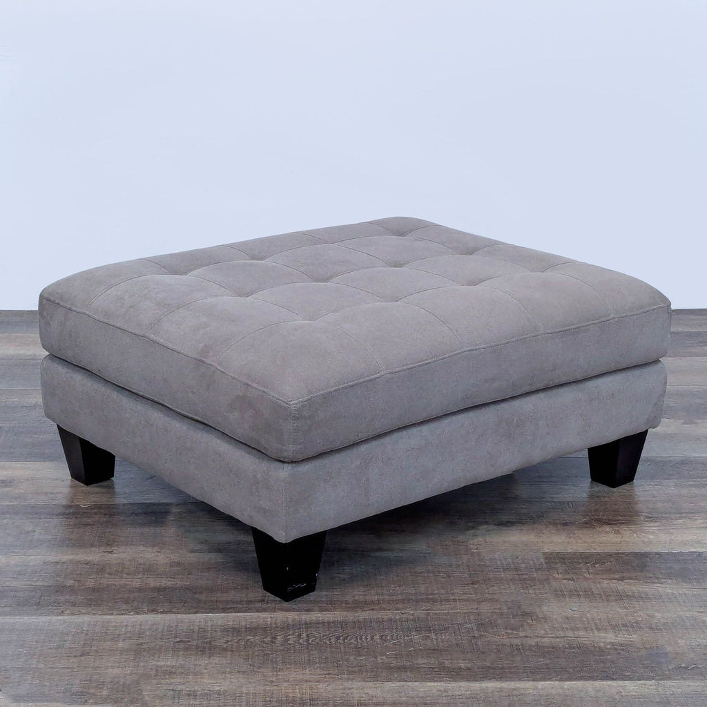 Gray rectangular ottoman with tufted top and dark wooden legs.